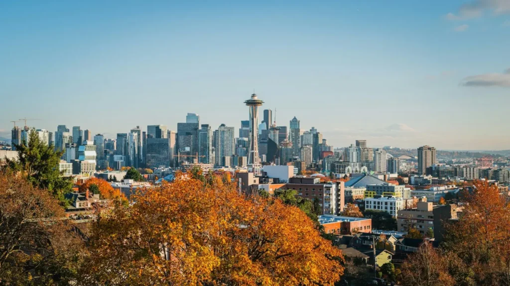 A panoramic view of Seattle's skyline during the fall, with vibrant autumn colors in the foreground.