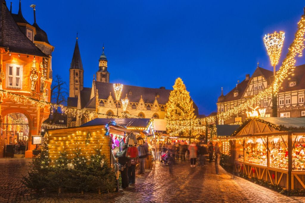 A festive European Christmas market glowing with lights, stalls, and a towering decorated tree at dusk.